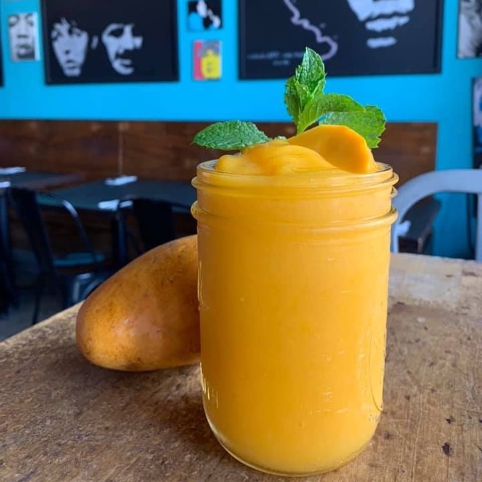 A mango smoothie in a mason jar with mint and mango slices, next to a whole mango.