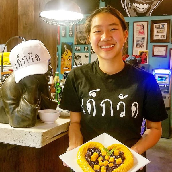 Smiling Wat Dong Moon Lek Noodle staff member holding a heart-shaped mango sticky rice dessert.