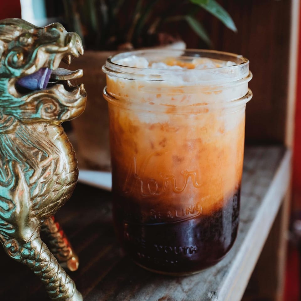 Thai iced tea in a mason jar next to a golden dragon statue.