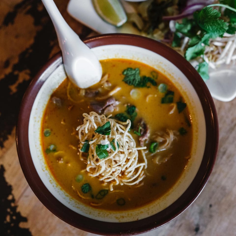 Overhead view of a bowl of Wat Dong Moon Lek Noodle's Thai curry noodle soup with crispy noodles.
