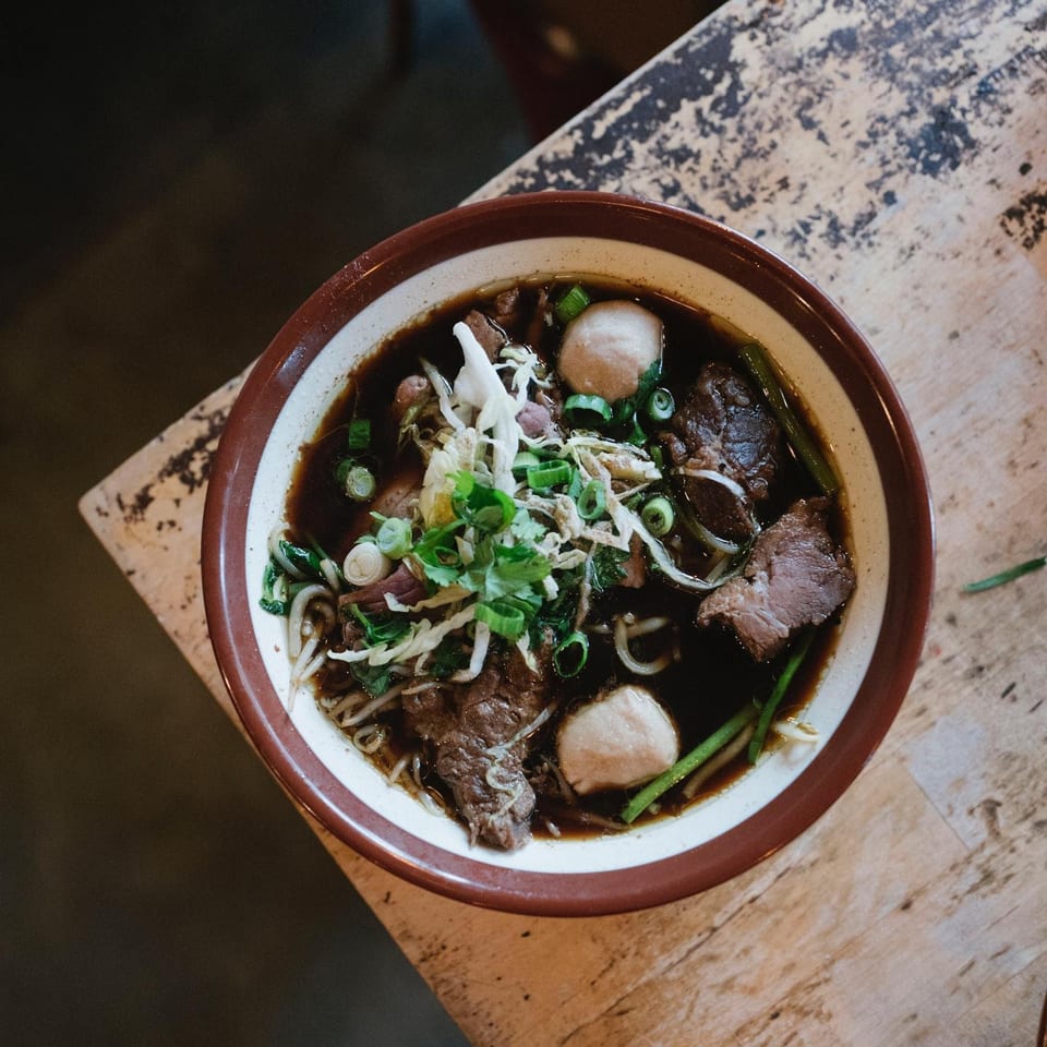 Overhead view of a bowl of Wat Dong Moon Lek Noodle's Thai beef noodle soup with meatballs.