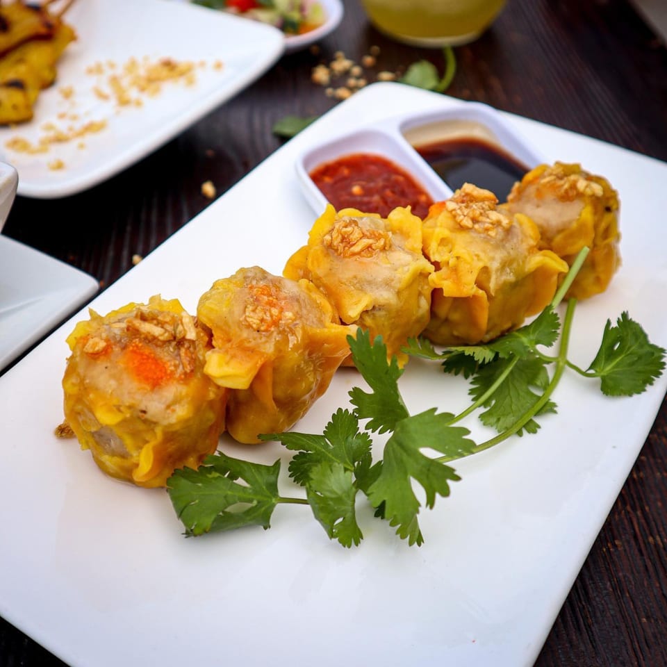 Five Thai dumplings with cilantro and two dipping sauces on a white rectangular plate.