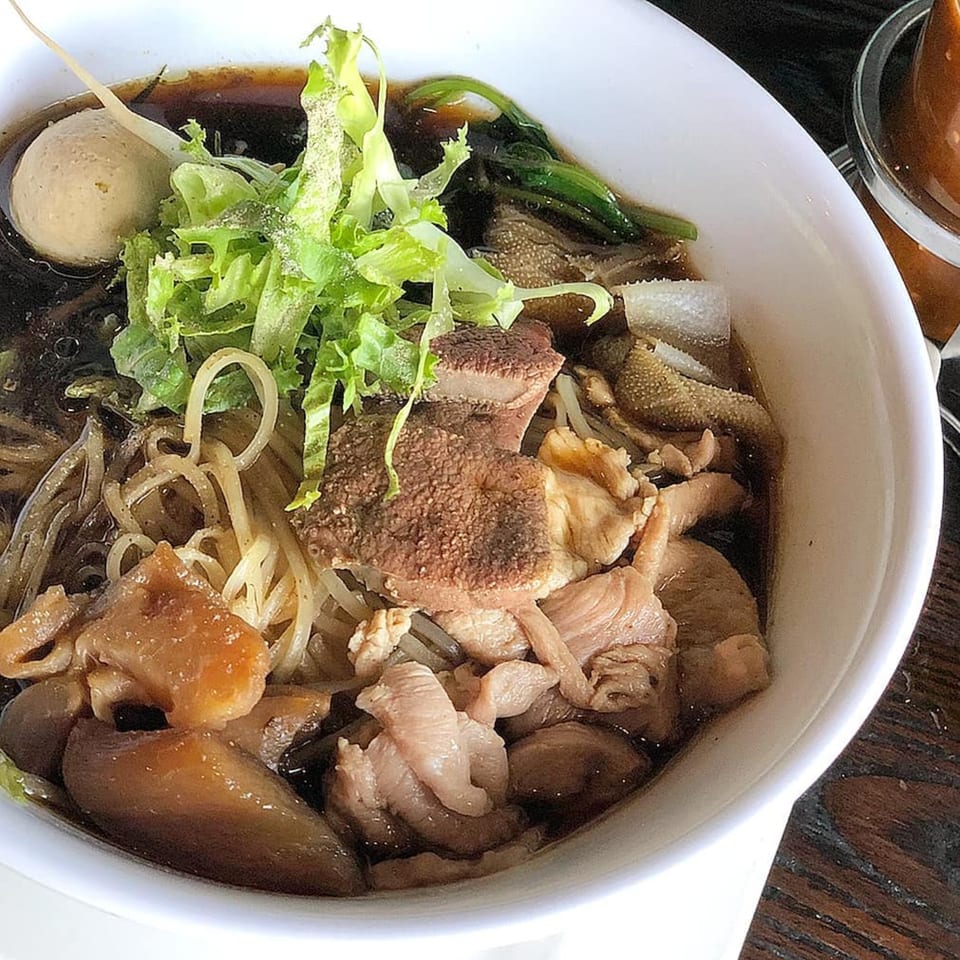 Close-up of a bowl of Wat Dong Moon Lek Noodle's Thai beef noodle soup with various meats and greens.